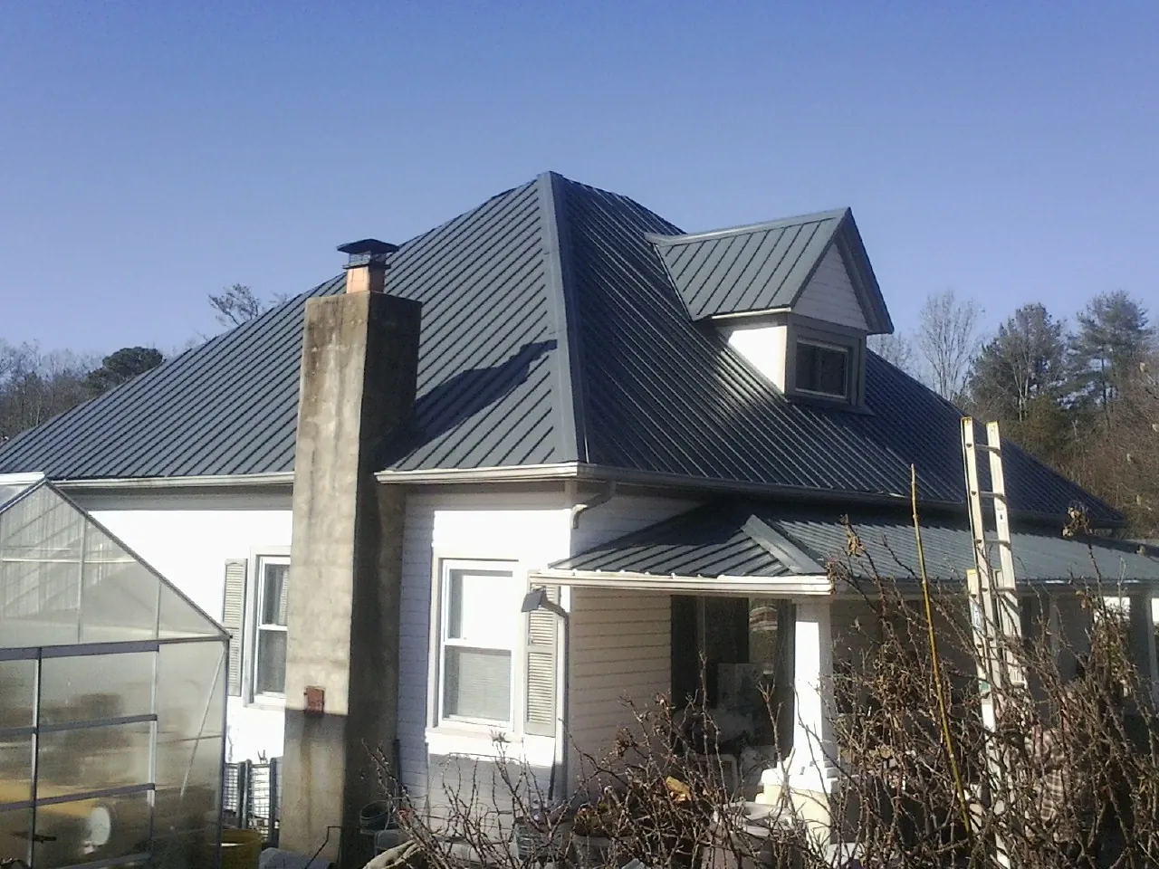 Dark blue standing seam metal roof on a white farmhouse with dormer — Slate & Tile Roof Repair by Roofing Brothers in Colebrook