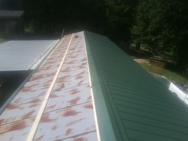 Old rusted panels beside newly installed green metal roofing — Wind Damage Roof Repair by Roofing Brothers in Colebrook