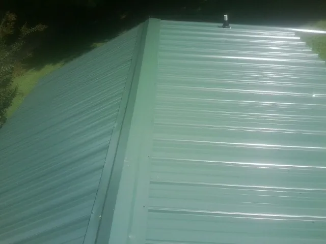 New green metal panels meeting at the ridge of a roof — Flat Roof Repair work by our crew in Colebrook