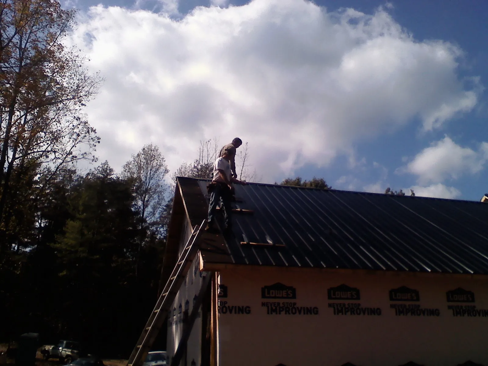 Roofer fastening dark metal panels high against a cloudy sky, from a Roof Inspection job in Colebrook
