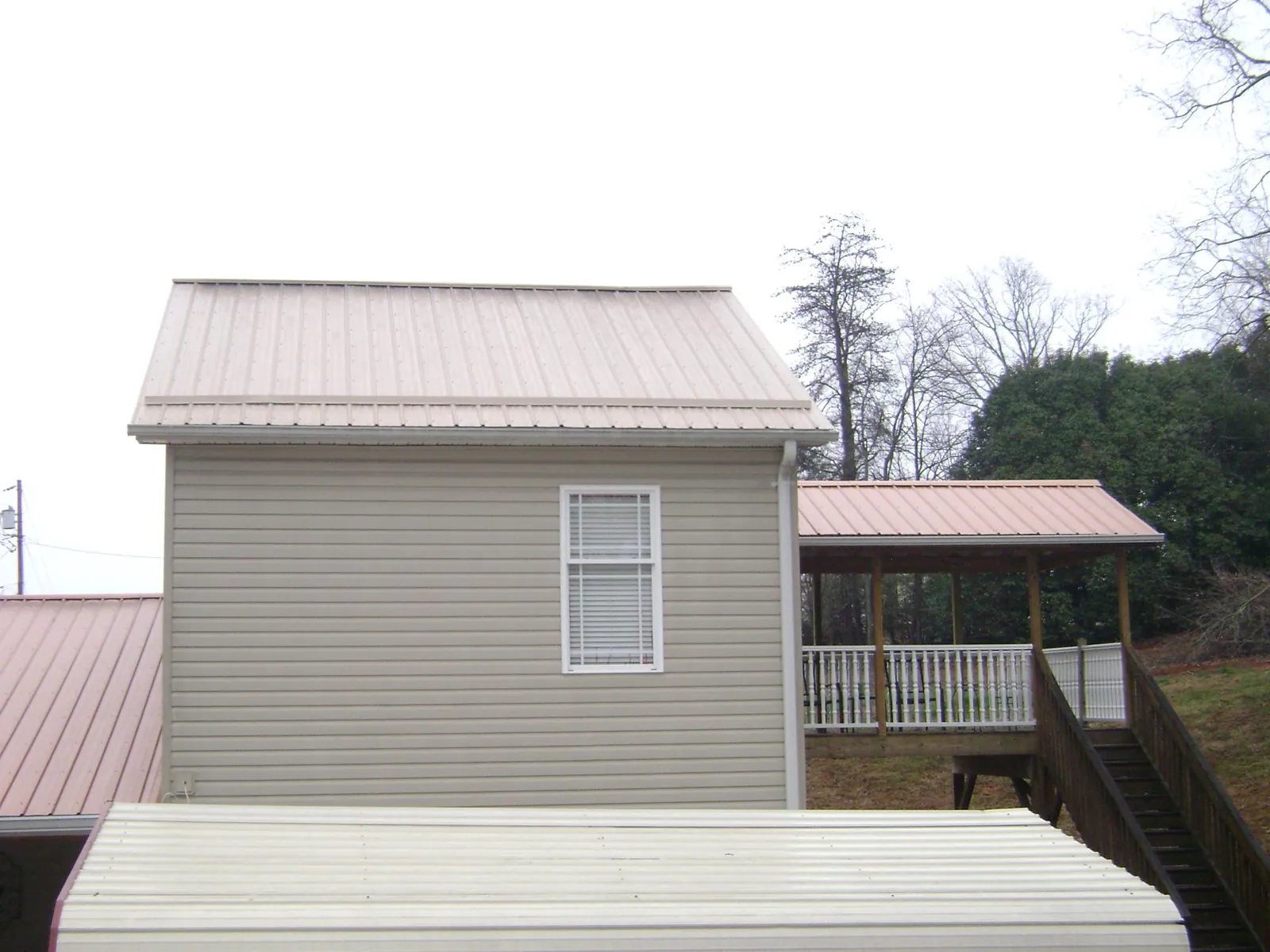Tan metal roofs on a two story addition and attached porch, from a Roof Replacement job in Colebrook